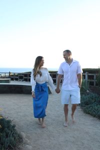 A man and woman holding hands while walking on the beach.