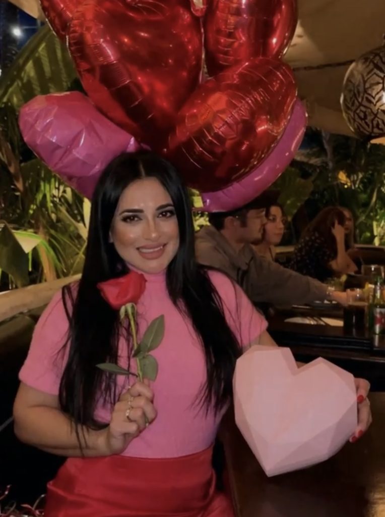 A woman holding a rose and heart shaped box.