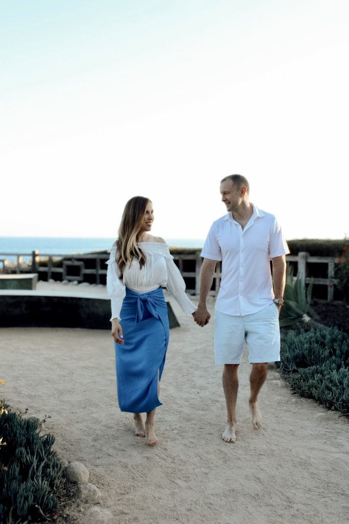 A man and woman holding hands while walking on the beach.